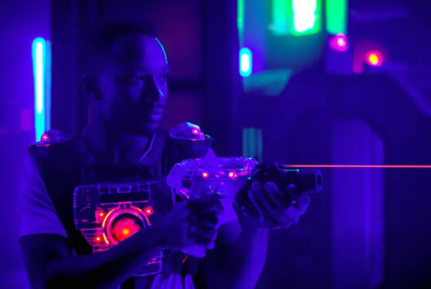 Photo of laser tag game player shooting light gun science fiction vest in black light
