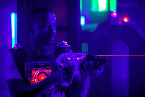 laser tag player holding gun shooting light in black light labyrinth