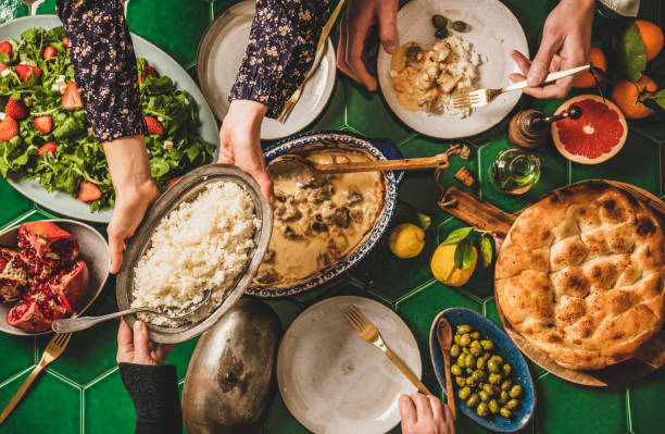 People passing Turkish foods over celebration dinner table, top view Family having Turkish dinner. Flat-lay of people passing rice pilav over green table with lamb in yogurt sauce, fresh arugula and strawberry salad and flatbread, top view. Ramazan iftar supper restaurant table layout stock pictures, royalty-free photos & images