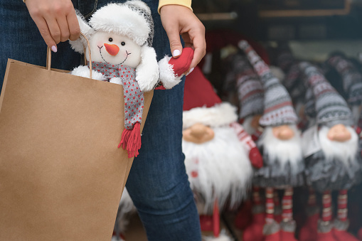 A female hands carries a paper bag with a Christmas toy snowman in the store. Concept of New Years discounts. Copy space and template, mock up