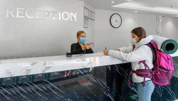 junge frau trägt schützende gesichtsmaske beim check-in an der hotelrezeption - hotel reception hotel key travel credit card stock-fotos und bilder