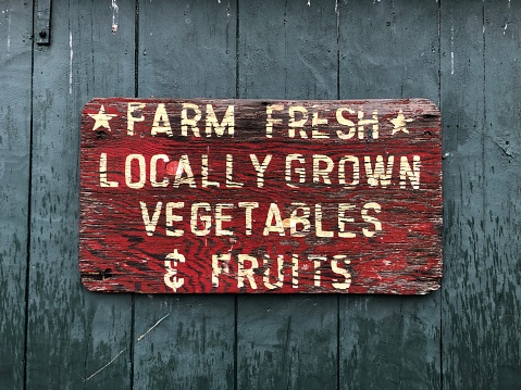 A rustic, weathered Farm Fresh Locally Grown Vegetables & Fruits Sign at a farm stand.