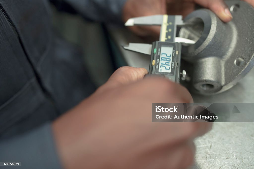 Hands detail of black man worker measuring machinery part with digital caliper at factory. Caliper Stock Photo