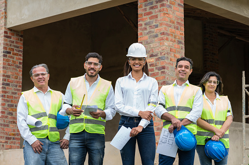 Group of ethnic engineers and builders working on a construction site. They all appear together looking at the camera and with a female engineer leading the team.
