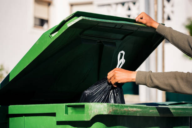 mann wirft schwarze umweltfreundliche recycelbare mülltüte in großen kunststoff grünen müllcontainer. nehmen sie den müll - garbage bag garbage bag garbage dump stock-fotos und bilder