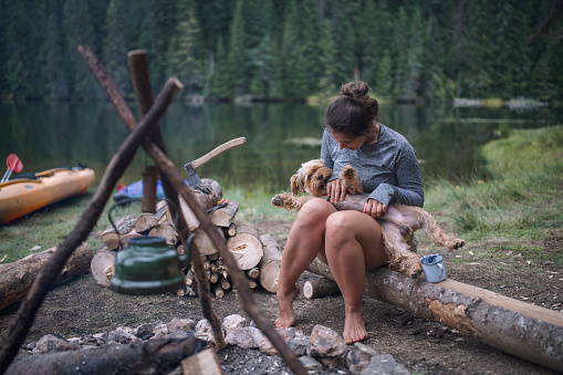 Young woman and her terrier dog are having fun playing and hugging while on camping in the nature