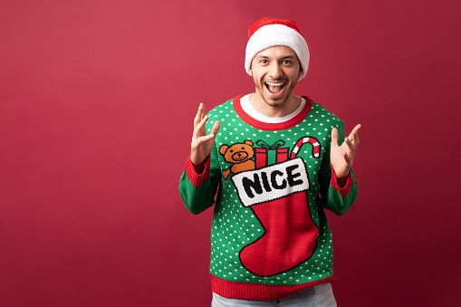 Portrait of a good looking man wearing an ugly sweater and santa hat and looking super excited about Christmas