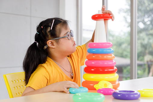 Girl with Down's syndrome play colorful toy at school. Concept disabled child learning in school.