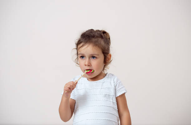 istock A small girl on a bright background stands and eats a lollipop. Isolated. 1281743271
