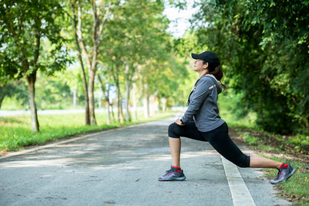 mulher saudável se aquecendo esticando as pernas na estrada ao ar livre. mulher corredora asiática treino antes do fitness e correr no parque. conceito de estilo de vida de cuidados de saúde. - passadeira via pública - fotografias e filmes do acervo