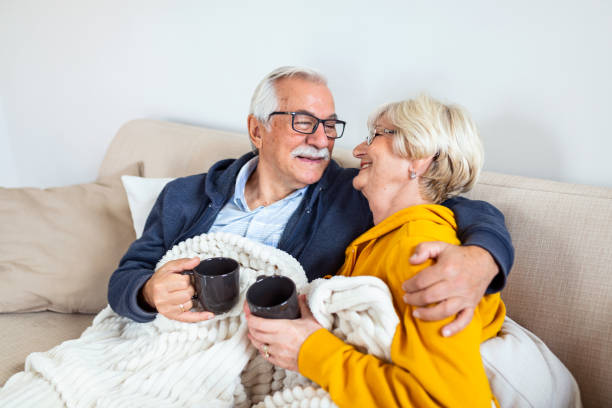 istock Happy old couple sitting on the sofa. Feeling cozy,drinking coffee or tea 1281745530