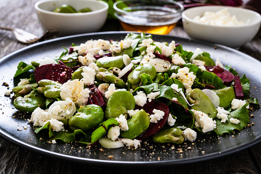 Beetroot salad with broad bean and goat cheese on wooden background