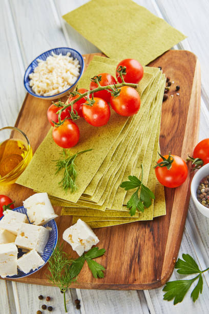 istock Sheets for making lasagna with spinach and ingredients: cherry tomatoes, cheese, butter, peppers and herbs 1281754278