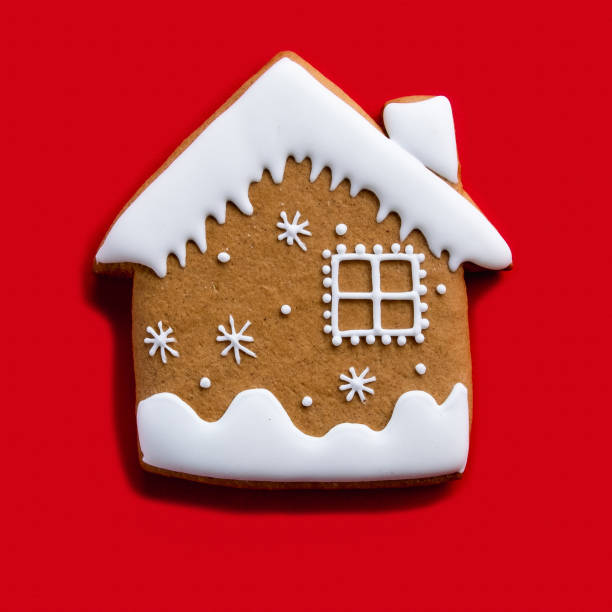 Gingerbread house. Christmas biscuit. Festive bakery food. Winter holidays ornament. Brown homemade cookie with white snow icing decoration isolated on red background.