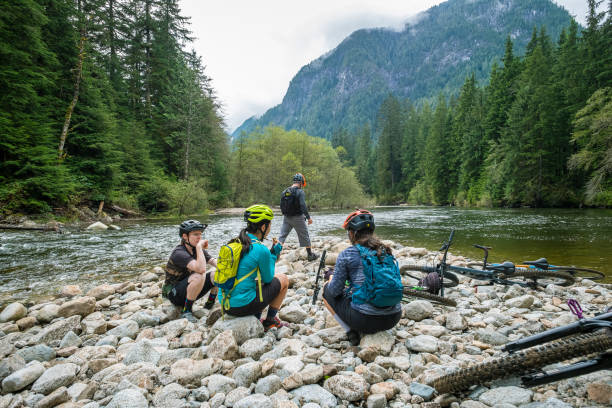 Multi-Ethnic Mountain Bikers Having Picnic Lunch on Riverbed in Forest