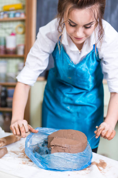 istock Pottering Ideas and Concepts. Smiling Female Professional Worker Preparing a Piece of Clay Using Special Wire in Professional Workshop.Vertical Image 1281757314