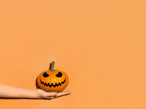 istock Halloween pumpkin in hand on orange background. 1281757783