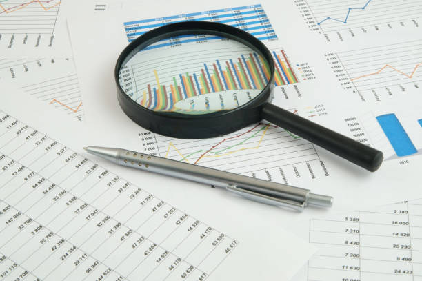 istock Magnifying glass and pen on financial charts and graphs 1281758115
