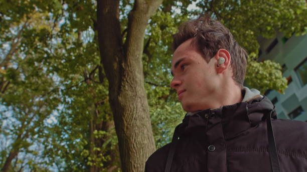 istock Young man talking on the phone using wireless headphones outdoors while walking down the street. young guy, teenager wears modern wireless headphones. Portrait of a young man 1281758136
