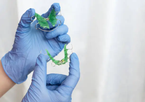 dentist's hands in blue medical gloves hold green children's orthodontic plaques for orthodontic bite correction, healthcare concept