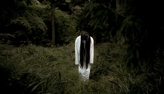 A creepy long black hair Japanese ghost woman in a dark forest.