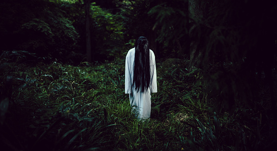 A creepy long black hair Japanese ghost woman in a dark forest.