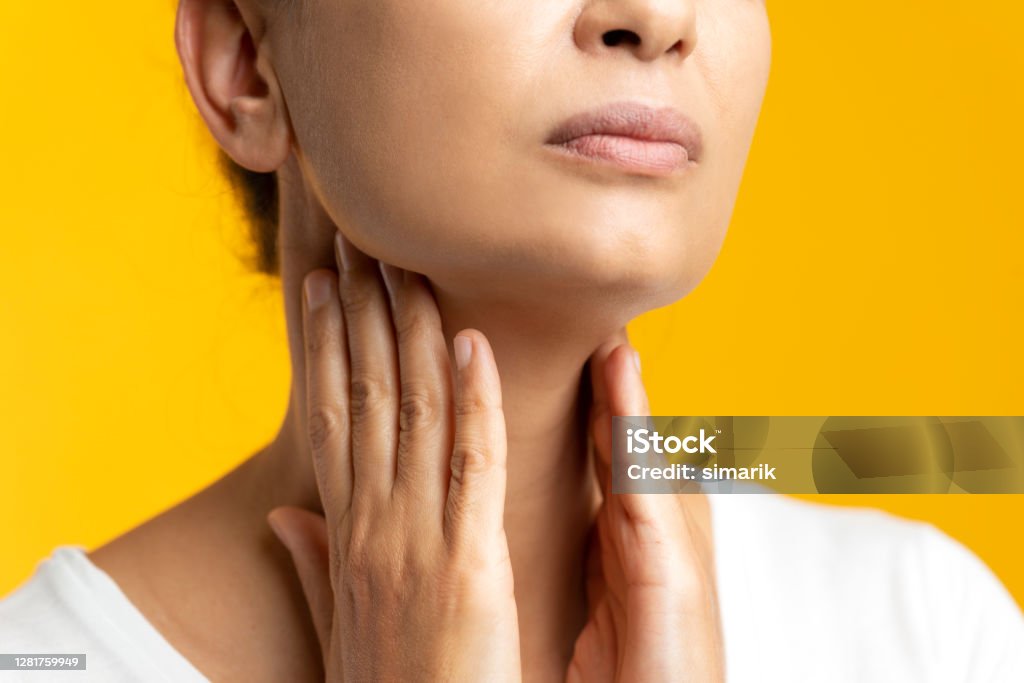 Throat Pain Unrecognizable female is holding her throat in pain in front of yellow background. Thyroid Gland Stock Photo