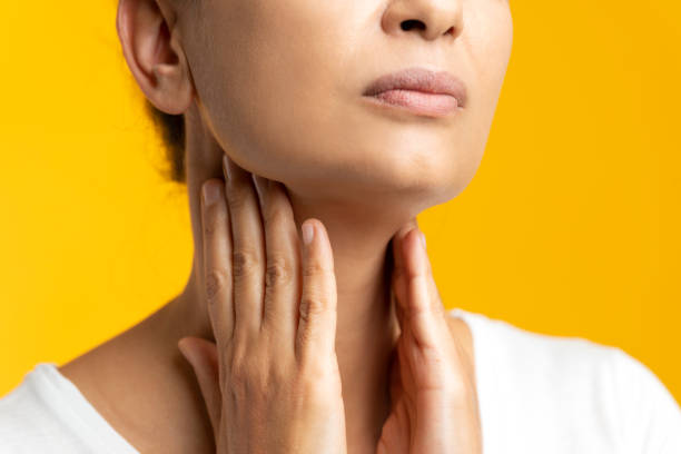 Throat Pain Unrecognizable female is holding her throat in pain in front of yellow background. thyroid gland stock pictures, royalty-free photos & images