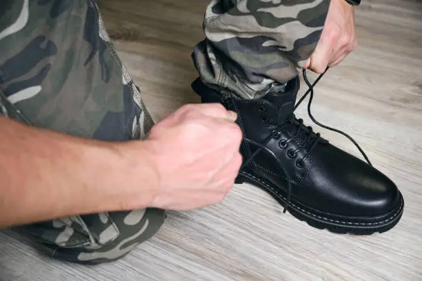 Man in a military uniform ties the laces on his black shoes