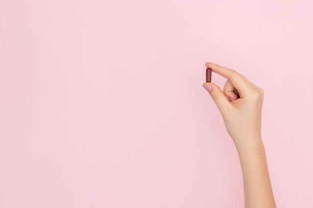 Hand with a pill in a capsule on a light pink background. stock photo