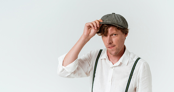 Country Caucasian guy wearing white shirt and suspenders straightens his cap.