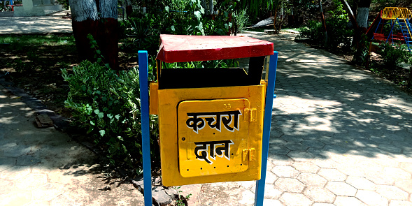 Indian yellow color dustbin with hindi text written Garbage donation on public park.