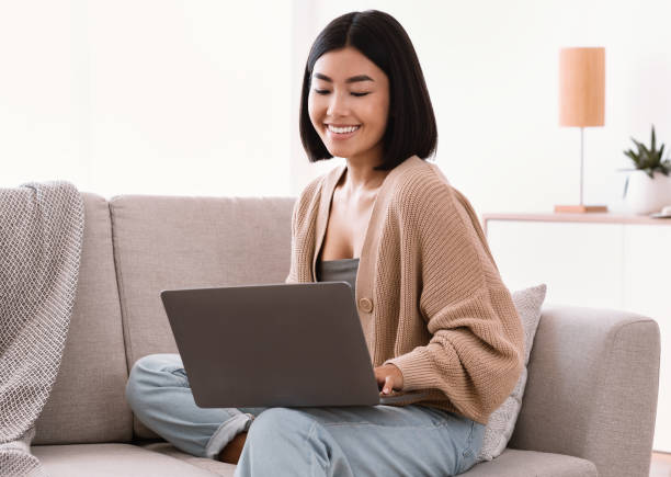 istock Asian woman sitting on couch and working on pc 1281768397