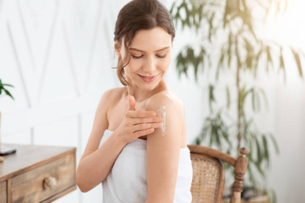 istock Happy young lady wrapped in towel moisturizing her skin 1281768402