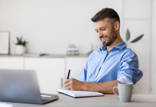 istock Smiling Handsome Businessman Taking Notes To Notepad At Workplace In White Office 1281768496