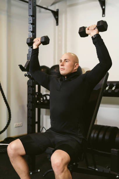 istock Bald muscular man training his shoulders with dumbbells in a public gym 1281770465