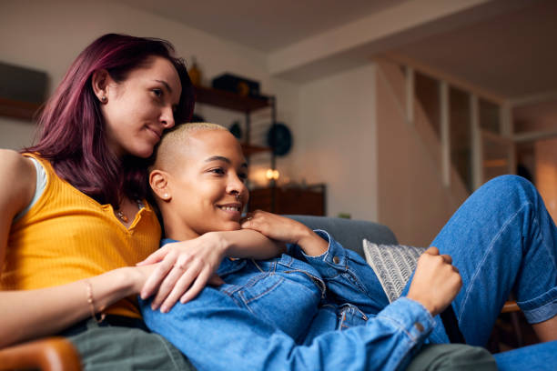 愛する同性の女性カップルは、自宅でソファに横たわってテレビを見て、一緒にリラックス - レズビアン ストックフォトと画像