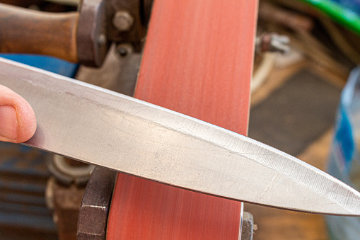 afilado pulido cuchilla de la cocina en el equipo de la lijadora de la correa. Fabricación de cuchillos. photo