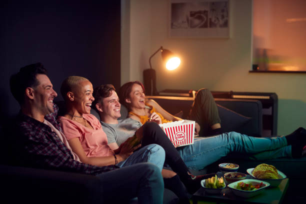 grupa przyjaciół jedzących popcorn siedzący na kanapie w domu oglądając wieczorny telewizor i relaksując się razem - movies at home zdjęcia i obrazy z banku zdjęć