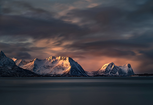 Beautiful view on Norwegian sea and snowcapped mountain range during winter golden hour in Steinfjord, Norway.