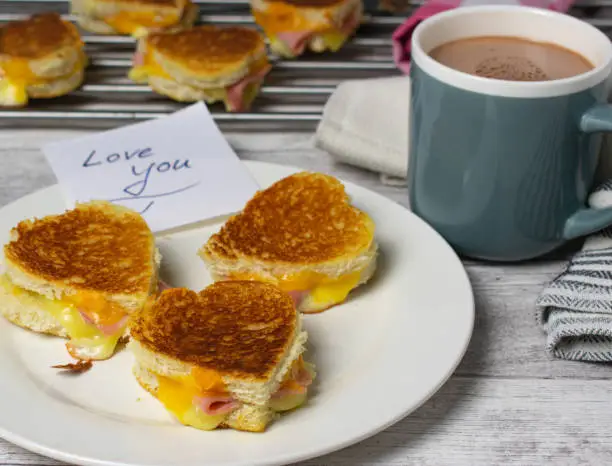 loving heart shaped sandwich with grilled ham and cheese with I love you message on a sticky note and a mug of cacao - ready to eat
