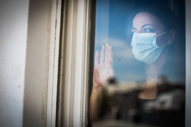 istock Woman wearing a surgical mask by a window 1281776889