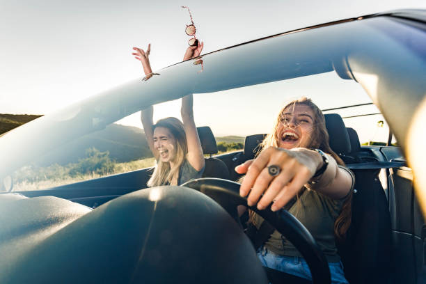 Cheerful female friends going on a trip in convertible car. Cheerful women having fun while screaming on a road trip in convertible car. The view is through windshield. singing stock pictures, royalty-free photos & images