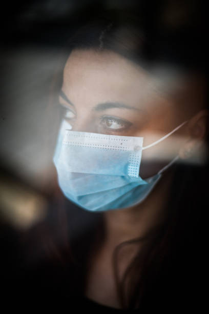 istock Woman wearing a surgical mask by a window 1281777192
