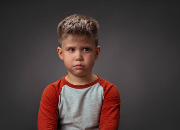 istock Sad boy looking at camera. Preschool kid expresses emotions. Isolated on gray background. Conflict concept. Copy space at right 1281778802