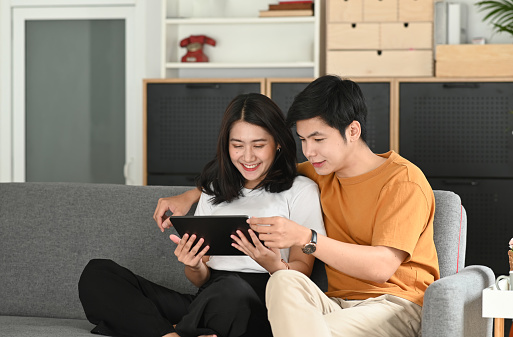 Happy young couple relax with tablet on comfortable couch and enjoy weekend at home.