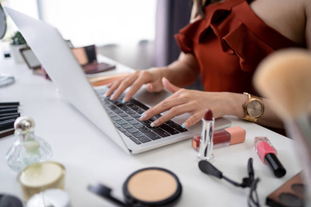 hermosa joven bloguera asiática utiliza un ordenador en la mesa. ella está comprando cosméticos en línea. - red lipstick fotografías e imágenes de stock