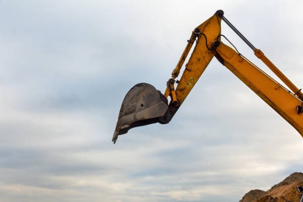 A raised hydraulic bucket of a yellow excavator against a cloudy sky background. Industrial construction machines
