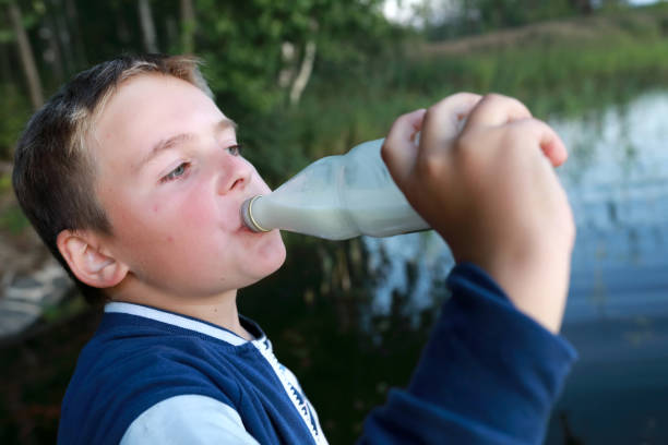 istock Boy drinking milk from bottle by lake 1281789032