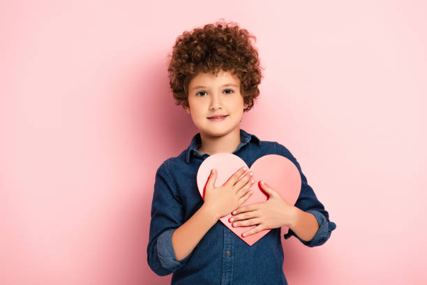 istock pleased boy holding heart shape paper cut on pink 1281789573